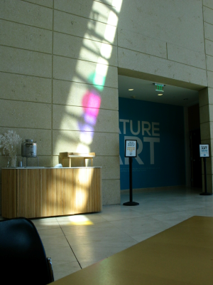 Next to the entrance of an exhibit, there is a line of light that shines down upon a bussing and trash station, at the edge of the photo are a table and chair.